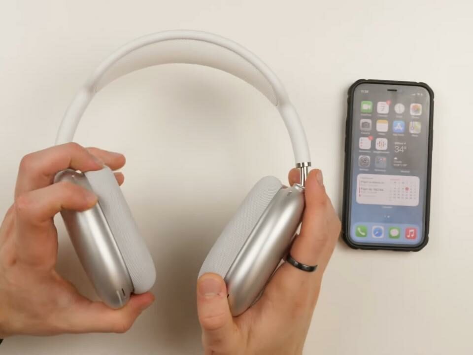 Las manos de un joven sosteniendo un par de AirPods Max plateados sobre una mesa