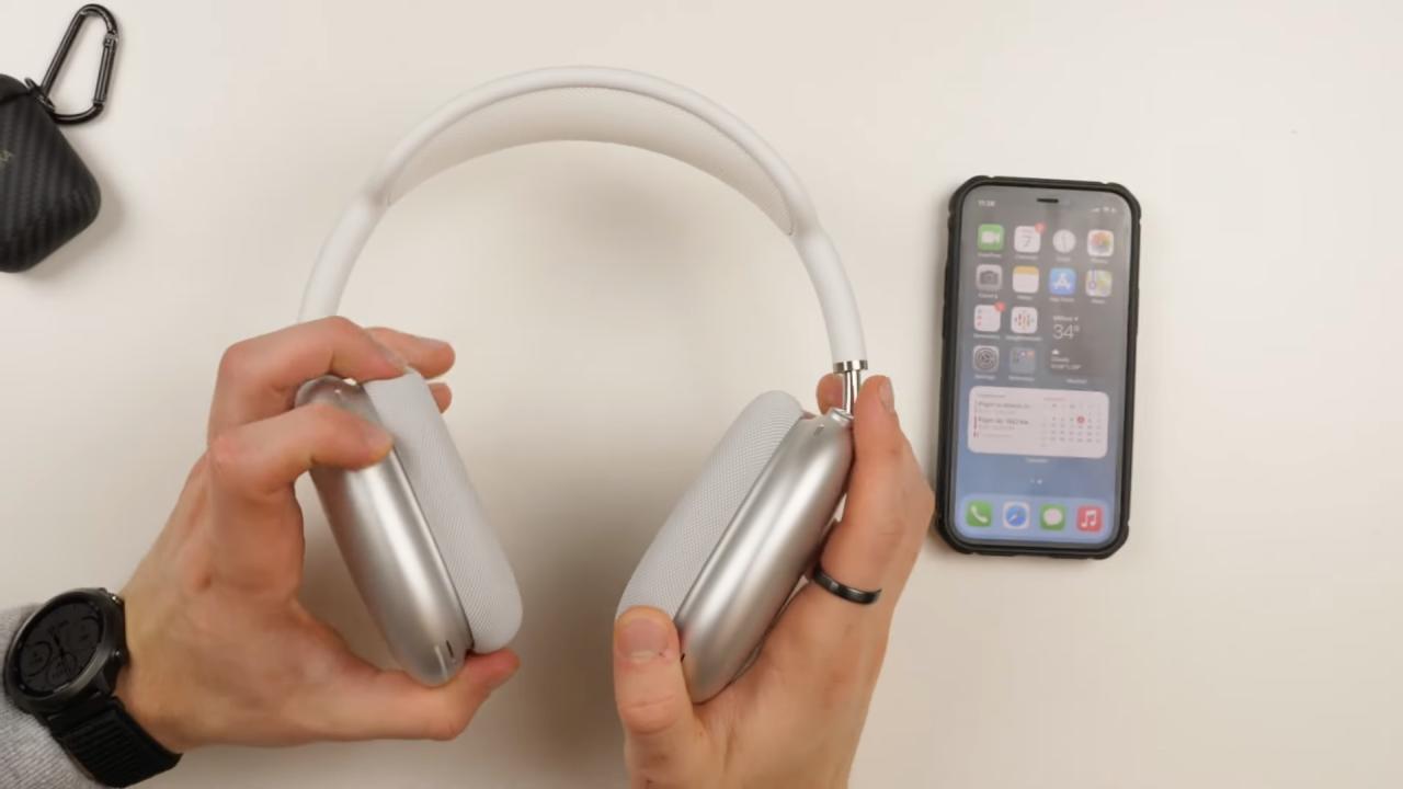 Las manos de un joven sosteniendo un par de AirPods Max plateados sobre una mesa