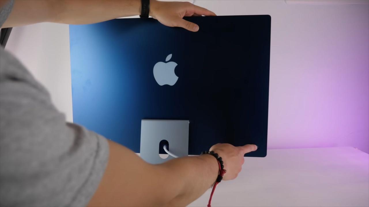 Una fotografía que muestra la parte trasera de una computadora Apple M1 iMac azul de 24 pulgadas con un dedo tocando el botón de encendido