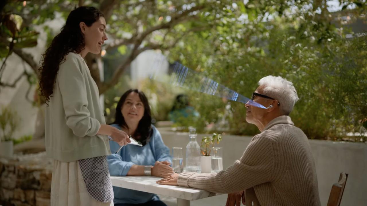 Una imagen fija del video de Apple que muestra a una persona mayor sentada en una mesa y hablando con una mesera usando sus AirPods Pro con la función Conversation Boost