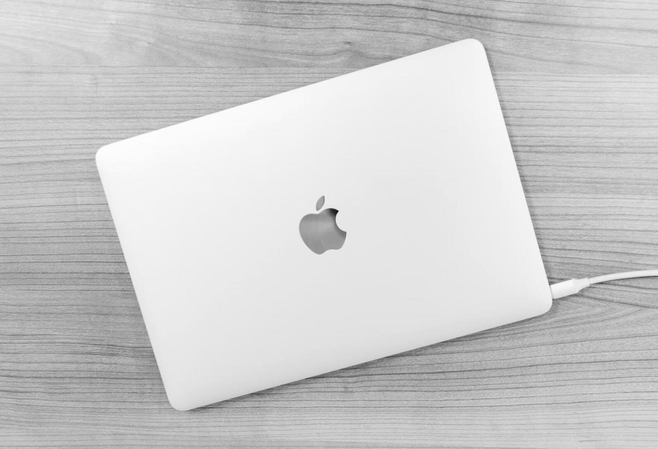 Imagen en blanco y negro de una MacBook en la mesa y cargándose
