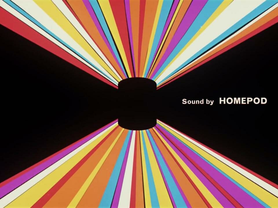 Una imagen tomada del video introductorio de Apple para HomePod, que muestra el parlante inteligente contra un fondo negro con rayas de luz de colores y el lema "Sonido de HomePod".
