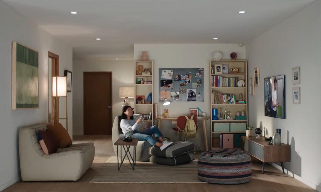 Una imagen de estilo de vida que muestra una casa con una mujer joven sentada en el sofá, sonriendo y viendo Apple TV y sosteniendo Siri Remote en su mano derecha