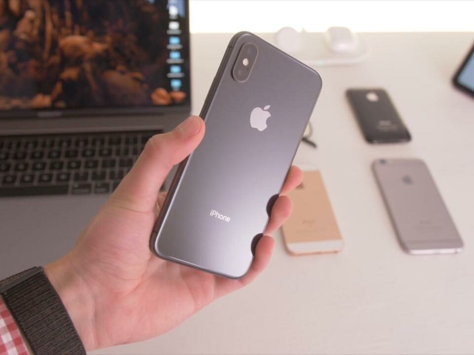 iPhone XS sostenido en la mano de un joven con un escritorio que se ve borroso en el fondo