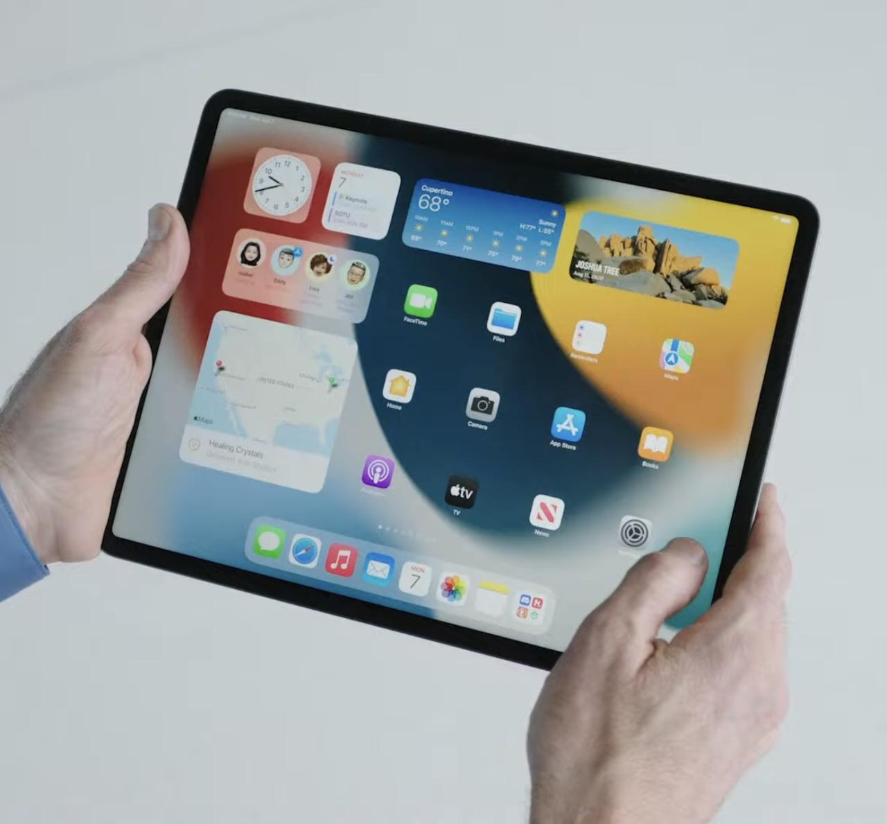 Una foto que muestra un iPad Pro sostenido en las manos con la pantalla de inicio mostrada con el widget Weather y otros widgets e íconos
