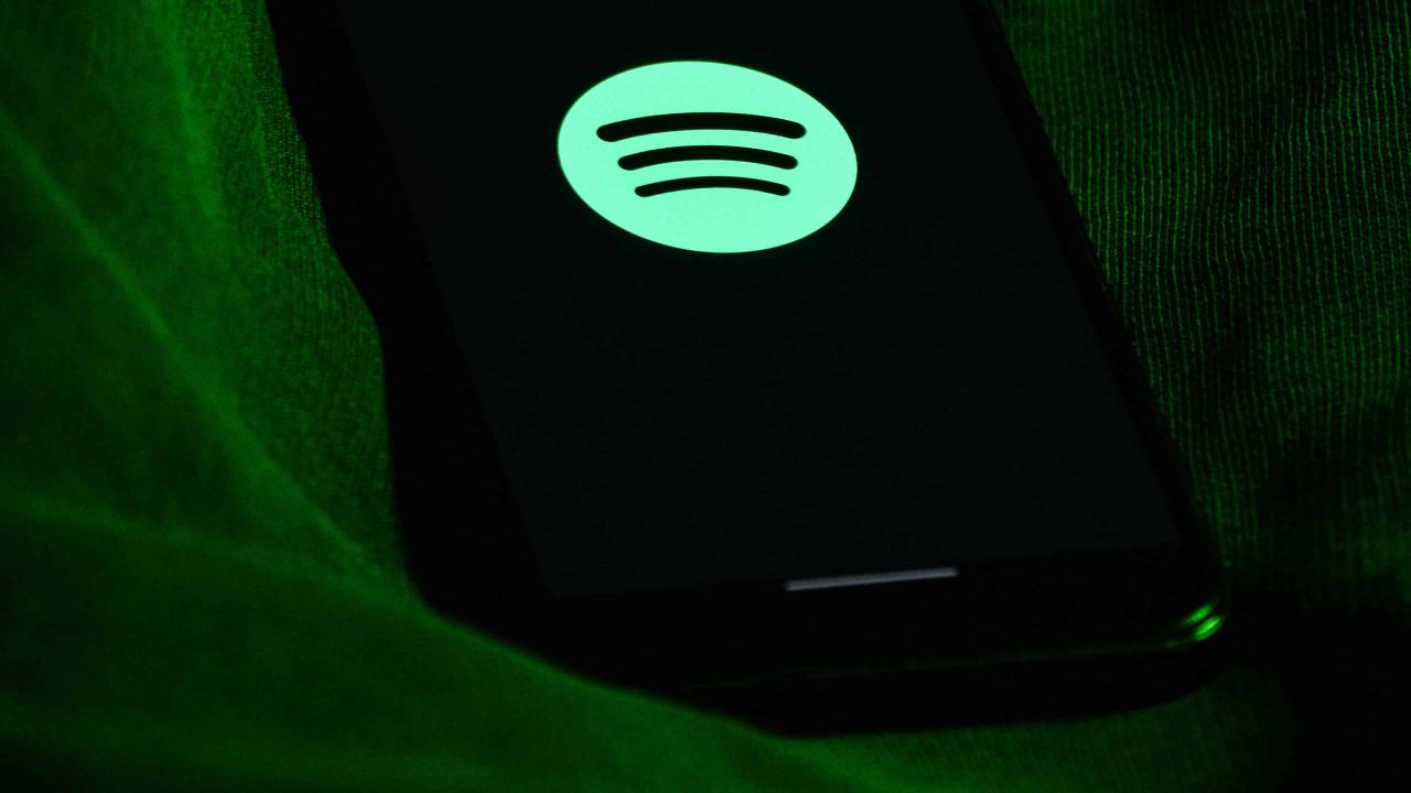 Una fotografía que muestra la parte trasera de un iPhone con un logotipo verde de Spotify en la pantalla, colocado boca arriba sobre un trozo de tela verde.