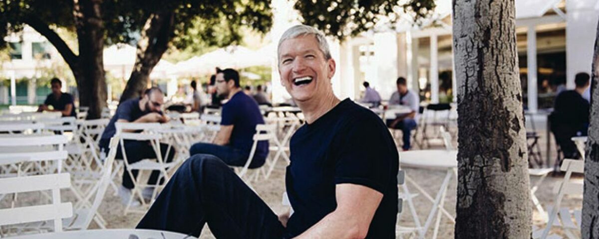 Tim Cook en la sede de Apple Park sentado en la entrada del edificio, sonriendo y mostrando sus bíceps
