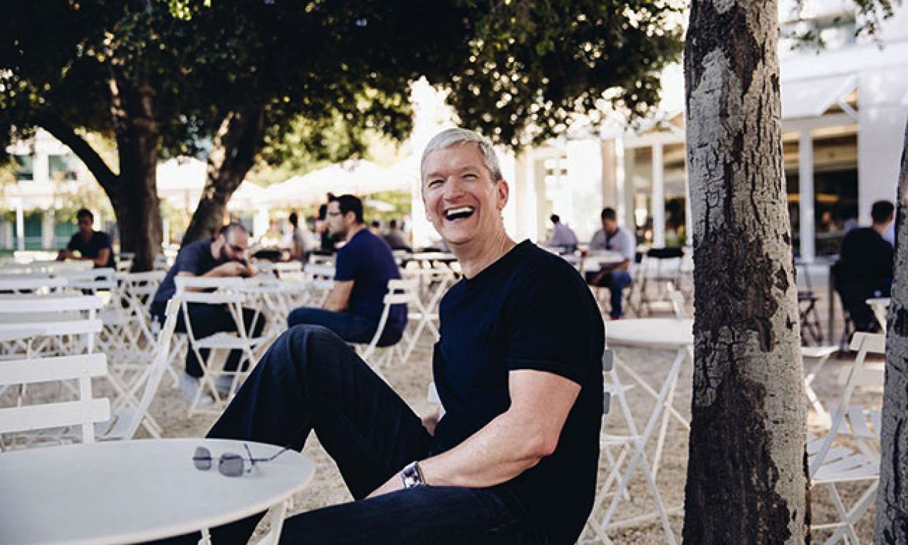Tim Cook en la sede de Apple Park sentado en la entrada del edificio, sonriendo y mostrando sus bíceps