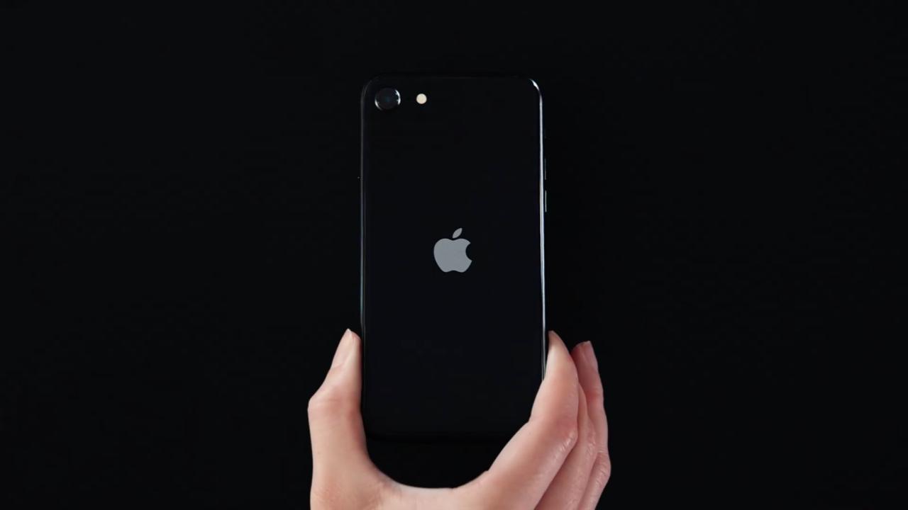 Fotograma del comercial de Apple para el iPhone SE que muestra una mano que coloca un iPhone SE negro mate sobre una superficie completamente negra