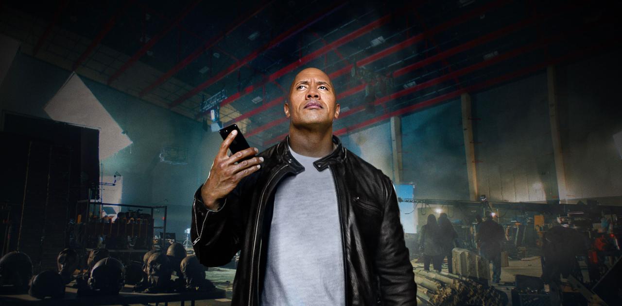Una foto que muestra al actor Dwayne Johnson sosteniendo un iPhone 7 Jet Black en la mano y conversando con Siri