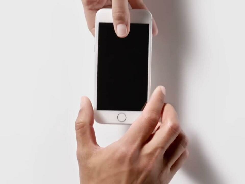 scene from Ap-in ad showing a male hand handing an iPhone 5s over to another male's hand