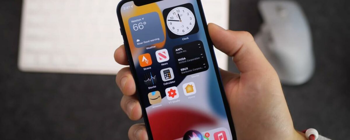 Una imagen que muestra la mano de un hombre joven sosteniendo un iPhone 13 con la pantalla de inicio de iOS 17